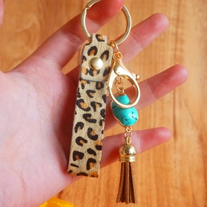 Portachiavi in pelle leopardata con pietra turchese e nappa in pelle marrone in mano