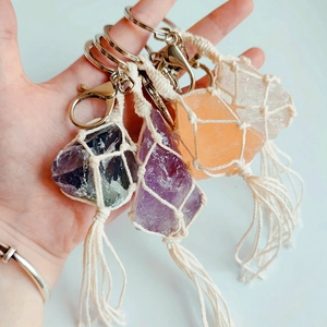 Hand-held view of four handmade macrame natural crystal gemstone keychains with tassels