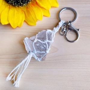 Macro shot of handmade woven net holding clear raw crystal with white tassel and metal keychain