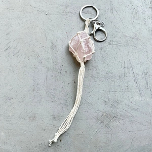 Handmade woven keychain featuring raw rose quartz stone with white cotton tassel and clasp