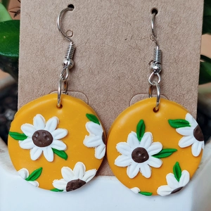 Detalle macro de pendientes de girasol hechos a mano con pétalos blancos y hojas verdes