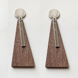 Dettaglio di orecchini geometrici in legno e metallo argento con texture naturali