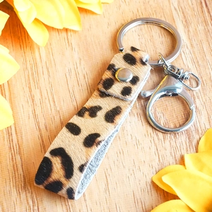 Close-up of leopard print pony hair leather keychain with silver hardware on a wood surface