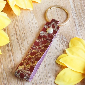Detail of leopard print leather keychain with gold hardware on a wooden background