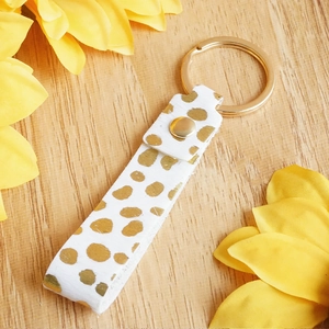 Genuine leather keychain with golden polka dots and metal ring on wooden background