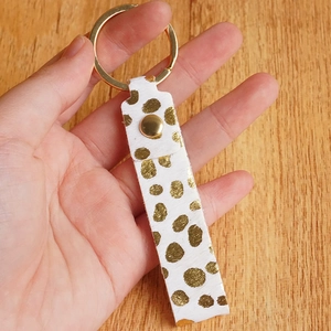 Hand holding genuine leather keychain with golden dots and horsehair texture