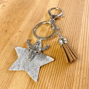 Detail of western cow skull keychain with brown leather fringe on rustic wood surface