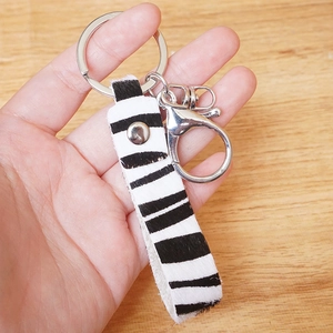 Handmade zebra print genuine leather keychain with silver metal rings on a wooden background