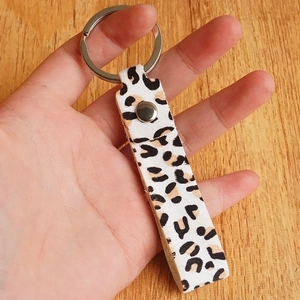 Handheld leopard print leather keychain with silver metal ring on wooden table
