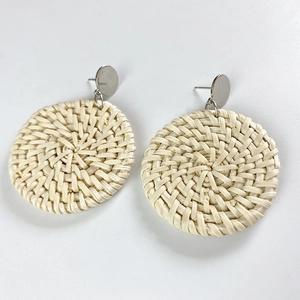 Close-up of handmade round rattan earrings with silver metal studs and woven texture