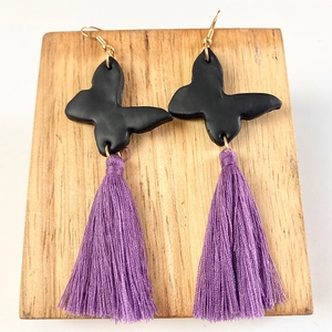 Black butterfly clay earrings with long purple silk tassels on a wooden display