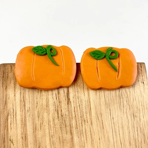 Detailed close-up of handmade orange pumpkin polymer clay earrings on a wooden stand
