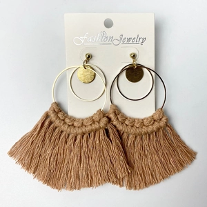 Detailed shot of golden hoop earrings featuring handmade tan tassel and woven fringe