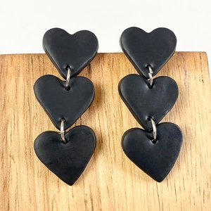 Close-up of black heart polymer clay drop earrings with matte finish and silver rings