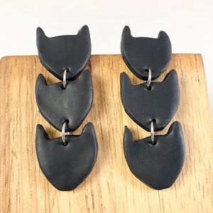 Close-up of black matte polymer clay earrings with triple cat-ear units and silver rings