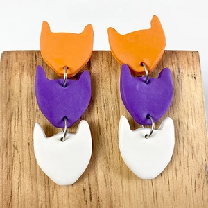 Detailed view of triple-layered cat clay earrings in orange, purple and white