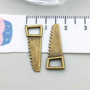 Detail view of two vintage bronze hand saw charms on a ruler showing 2.5cm size