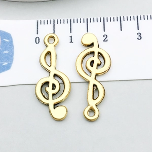 Détail de breloques clé de sol dorées vintage avec mètre ruban indiquant la taille 2,8cm