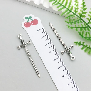Macro shot of two vintage silver sword charms with ruler showing 5.5cm size detail