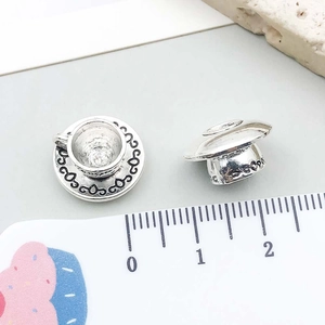 Macro detail of miniature silver teacup pendants showing 10mm scale and embossed texture