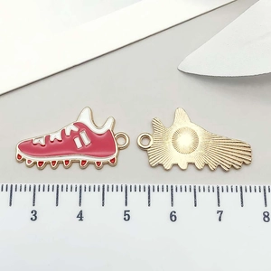 Dettaglio di ciondolo a scarpa da calcio in smalto rosso con retro dorato e righello
