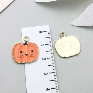 Detail of pumpkin enamel pendant with cartoon face next to scale for size reference