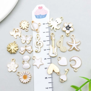 Various white enamel and gold alloy charms with ruler for size reference and scale