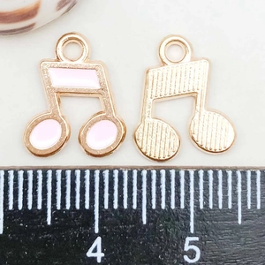Detailed view of enamel musical note pendants with ruler showing size and texture