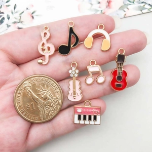 Detailed size comparison of enamel music charms with a coin in palm for DIY jewelry