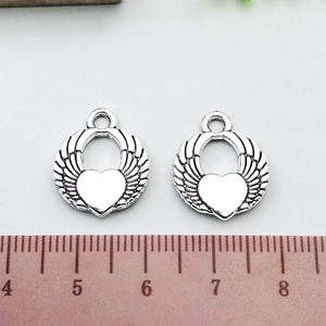 Detailed view of antique silver heart wing charms on a ruler showing 2.3cm scale