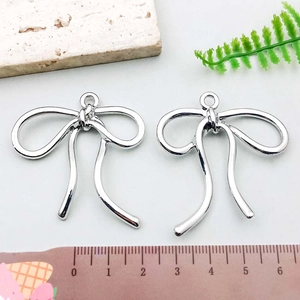 Close-up of polished silver bow pendants with measurements on a clean white background