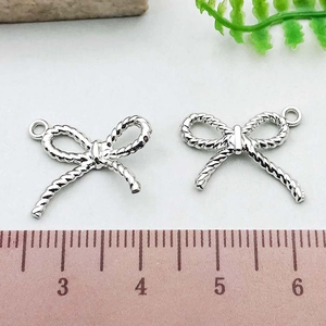 Close-up of silver bow pendant charms with rope texture design and scale measurement