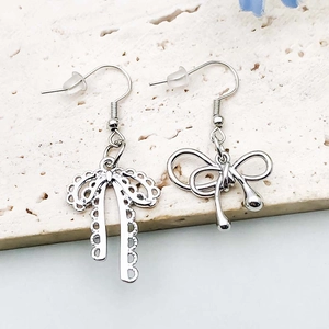 Detailed macro view of mismatched silver bow earrings on elegant cream stone surface