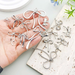 Silver bow pendants for DIY jewelry making shown in hand for size perspective