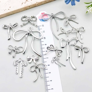 Silver bow alloy charms for DIY necklaces with ribbon and cutout patterns shown with ruler