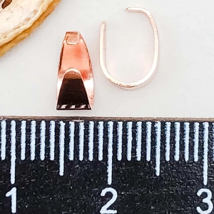 Macrodetail van roségouden knijpbeugels voor sieraden getoond met een meetliniaal