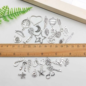 Assorted silver alloy charms set with wings and heart shapes shown with a wooden ruler
