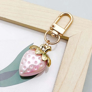 Macro detail of pink pearlized strawberry pendant with gold leaf and lobster clasp charm