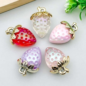Macro shot of colorful acrylic strawberry pendants for DIY jewelry with gold metal leaves