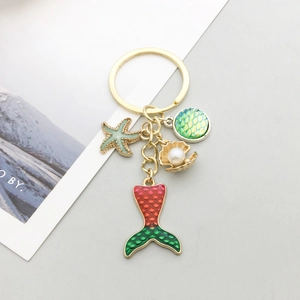 Porte-clés sirène doré avec étoile de mer verte et breloques coquillage sur fond gris