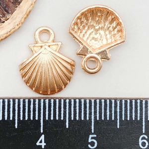 Macro shot of gold shell alloy charms with detailed fan-shaped textures and size scale