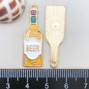Détail macro d'un pendentif bouteille de bière en émail jaune avec inscription 'BEER' dorée