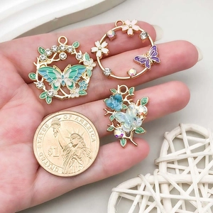Detail of three colorful enamel butterfly pendants with crystal inlay on hand with a coin