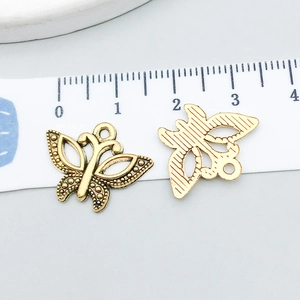 Detail view of antique gold butterfly charms with hollow design next to a measuring ruler