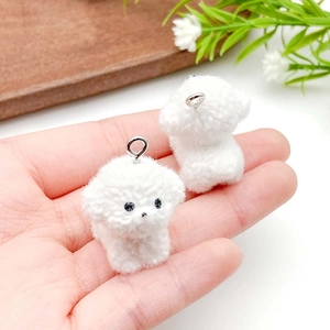 Detail showing two white flocked puppy charms held in hand for size visualization