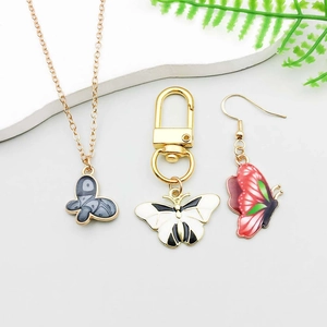 Détail des pendentifs papillon en émail sur collier, porte-clés et boucle d'oreille dorés