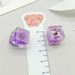 Macro detail of cube resin pendant with purple dried flowers and gold metal loop hook