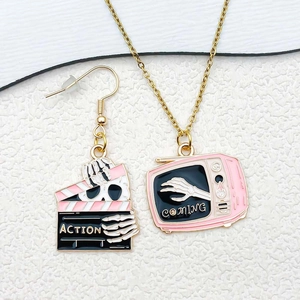 Macro shot of pink enamel clapperboard and TV charms with gothic skeleton hands detail