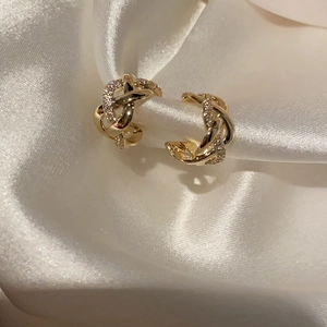 Elegantes pendientes de aro trenzados dorados con cristales sobre seda blanca