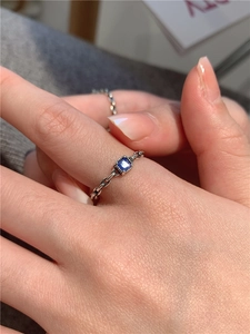 Détail de la bague en chaîne argentée avec pierre de zircon bleue carrée sur doigt